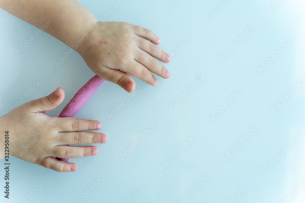 Little children's handles roll a sausage made of pink mass for modeling on a light surface. children's creativity Little children's handles roll a sausage made of pink mass for modeling on a light surface. children's creativity