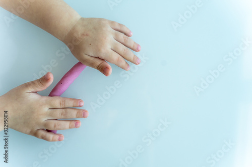 Little children's handles roll a sausage made of pink mass for modeling on a light surface. children's creativity