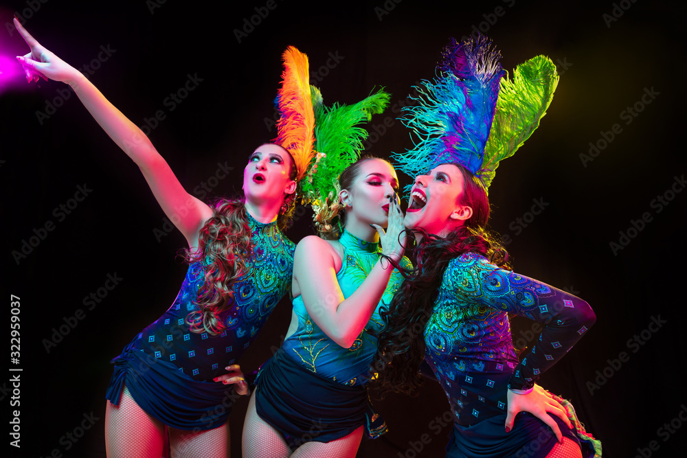 Feelings. Beautiful young women in carnival, stylish masquerade costume with feathers on black background in neon light. Copyspace for ad. Holidays celebration, dancing, fashion. Festive time, party. Feelings. Beautiful young women in carnival, stylish masquerade costume with feathers on black background in neon light. Copyspace for ad. Holidays celebration, dancing, fashion. Festive time, party.