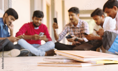 selective focus of Books, Group of students busy on mobile by avoiding books during exams at college - Teenager students on smartphone video game addiction concept.