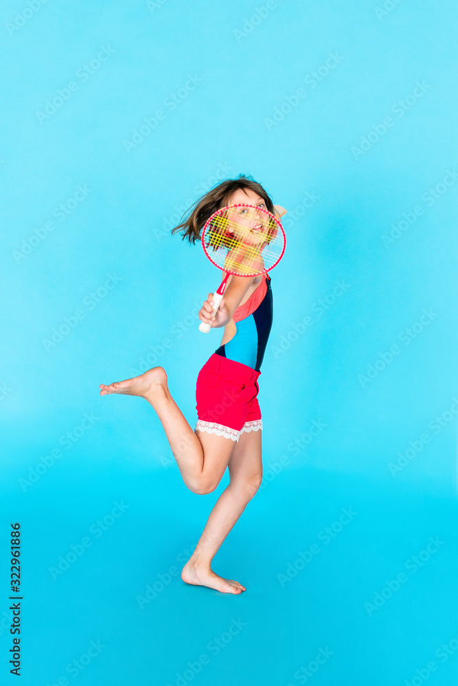Young teenager girl jumping and playing badminton on blue background