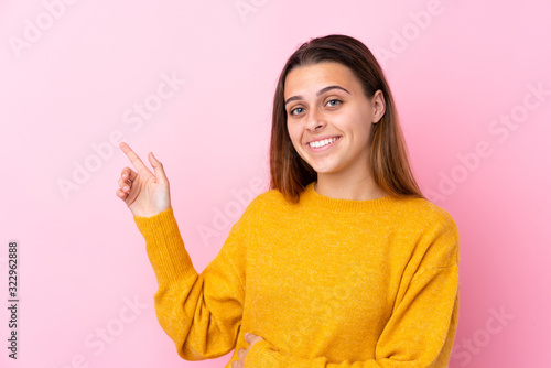 Teenager girl with yellow sweater over isolated pink background pointing finger to the side