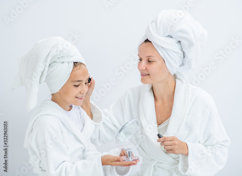 Happy family at home. Mother and young daughter applying makeup at home. Mom and child girl are in bathrobes and with towels on their heads