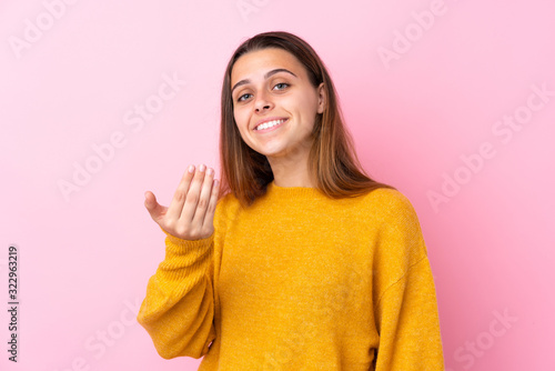 Teenager girl with yellow sweater over isolated pink background inviting to come with hand. Happy that you came