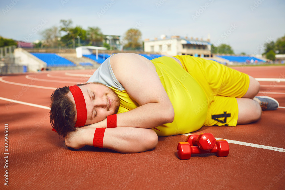 Fat lazy man sleeps tired lies on the track in the stadium. - obrazy, fototapety, plakaty 