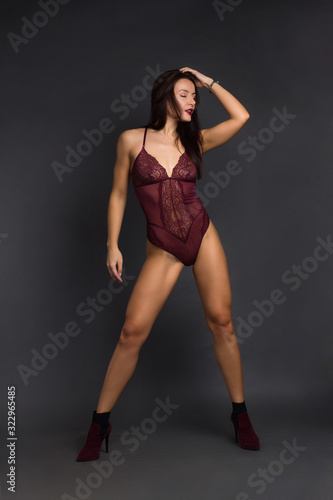 a brunette girl in Burgundy bodysuit poses and dances on a gray Studio background