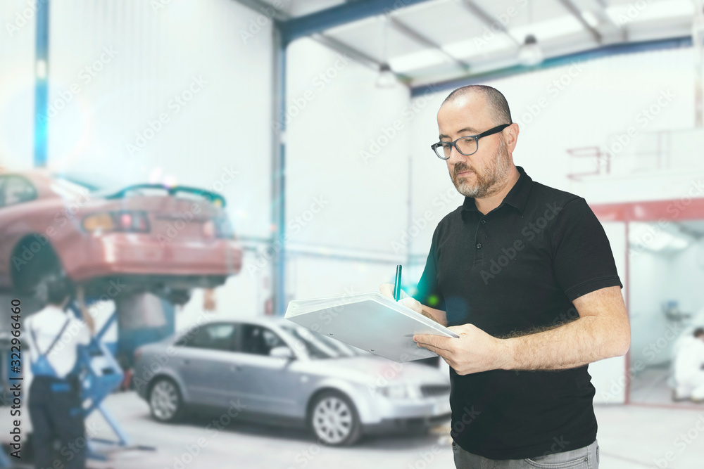 Young man with a check list for a car revision. Repair workshop with empty copy space for Editor's text. Young man with a check list for a car revision. Repair workshop with empty copy space for Editor's text.