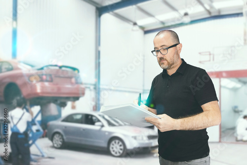 Young man with a check list for a car revision. Repair workshop with empty copy space for Editor's text.
