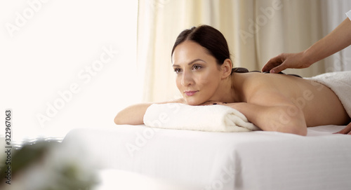Pretty brunette woman enjoying treatment with hot stones in spa salon. Beauty concept