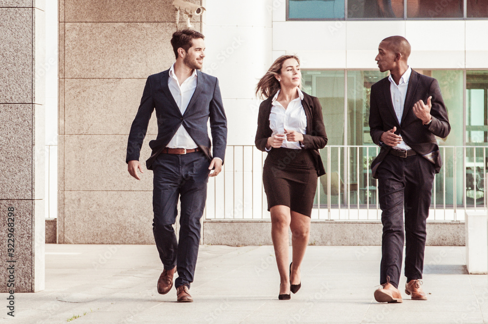Cheerful successful coworkers talking on their way to office. Business people walking outdoors and chatting. Friendly officemates concept Cheerful successful coworkers talking on their way to office. Business people walking outdoors and chatting. Friendly officemates concept