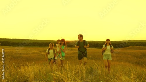 Travelers teamwork. happy family of travelers ascends to their victory, to top of the hill. tourists children and mom and father with backpacks climb mountain against backdrop of the beautiful sun.