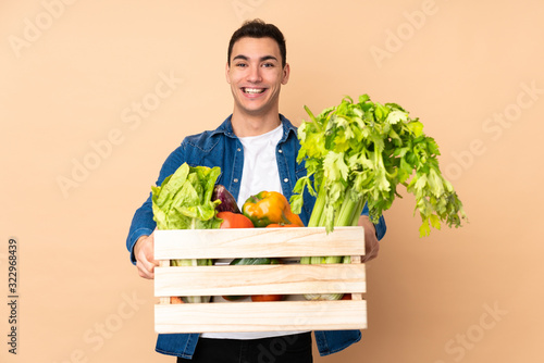Farmer with freshly picked vegetables in a box isolated on beige background