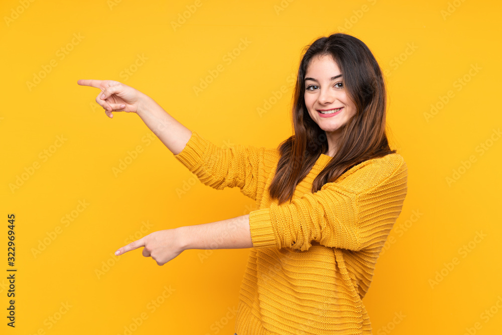 Young caucasian woman isolated on yellow background pointing finger to the side and presenting a product Young caucasian woman isolated on yellow background pointing finger to the side and presenting a product