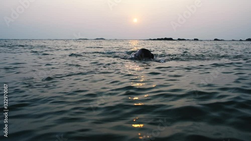 Young woman triathlon athlete swimming in open sea at sunset swimmer evening workout slow motion photo