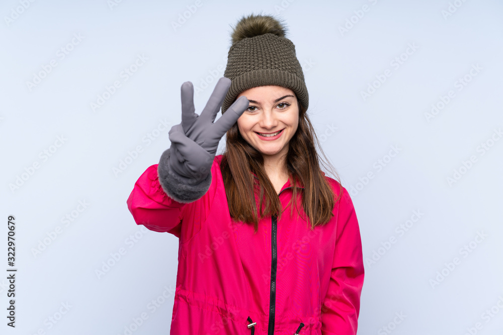 Young girl with winter hat isolated on blue background happy and counting three with fingers Young girl with winter hat isolated on blue background happy and counting three with fingers