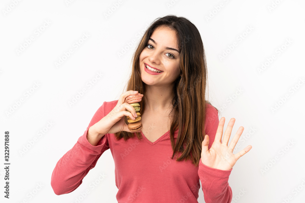Young caucasian woman isolated on pink background holding colorful French macarons and saluting