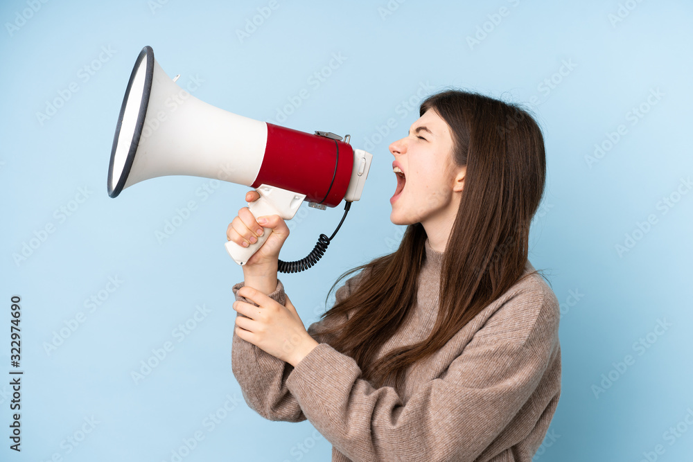 Young Ukrainian teenager girl wearing a sweater over isolated blue background shouting through a megaphone Young Ukrainian teenager girl wearing a sweater over isolated blue background shouting through a megaphone