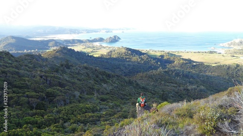 Hiker is sitting on a rock and enjoys the awesome view of the Island with the valley, forest and Ocean