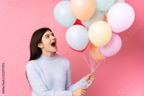 Young Ukrainian teenager girl holding lots of balloons over isolated pink background