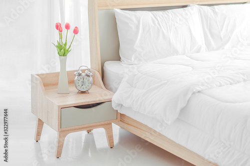 Close up of modern bed and bedside cabinet with clock and flower vase in the bedroom bedroom. bouquet on the nightstand