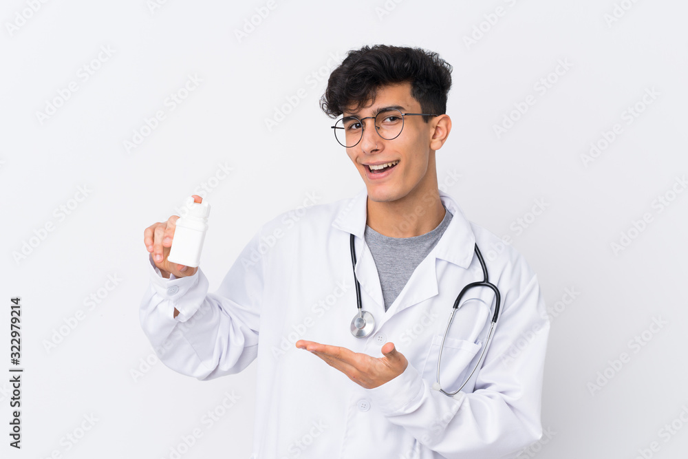 Young Argentinian man over isolated white background wearing a doctor gown and holding pills Young Argentinian man over isolated white background wearing a doctor gown and holding pills