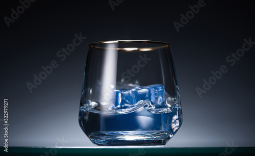 transparent glass with ice cubes and vodka in dark with blue back light