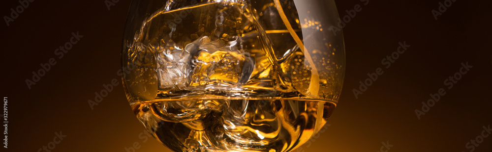 transparent glass with ice cubes and vodka in dark with warm back light, panoramic shot