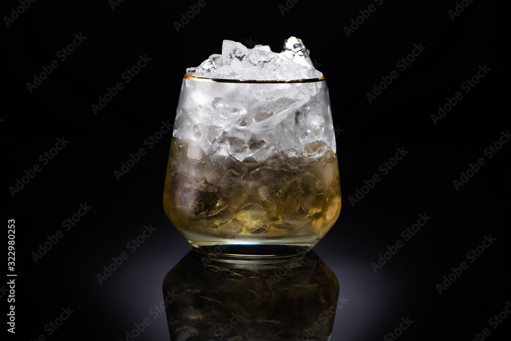 transparent glass with ice and golden liquid on black background transparent glass with ice and golden liquid on black background