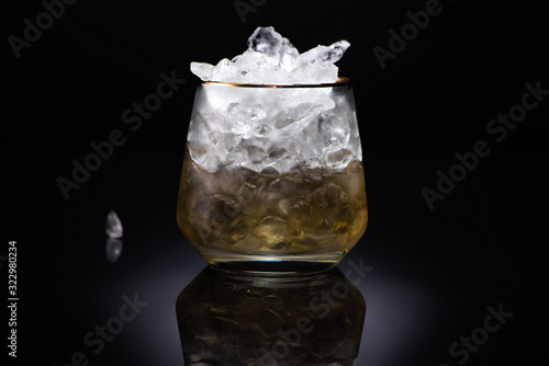 transparent glass with ice and golden liquid on black background