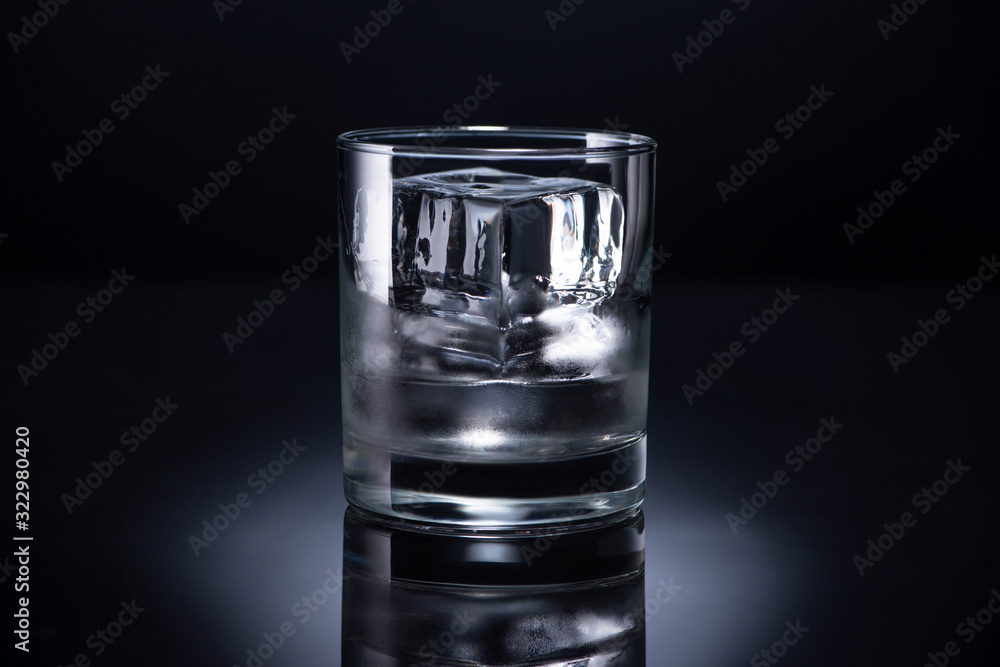 transparent glass with ice cube and vodka on black background transparent glass with ice cube and vodka on black background