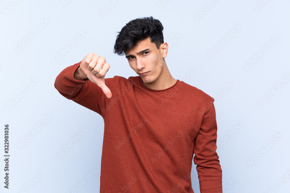Young Argentinian man over isolated blue background showing thumb down with negative expression Young Argentinian man over isolated blue background showing thumb down with negative expression