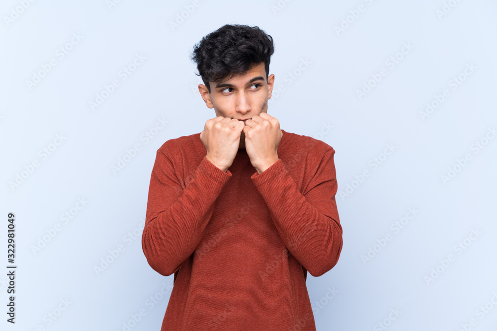 Young Argentinian man over isolated blue background nervous and scared putting hands to mouth Young Argentinian man over isolated blue background nervous and scared putting hands to mouth