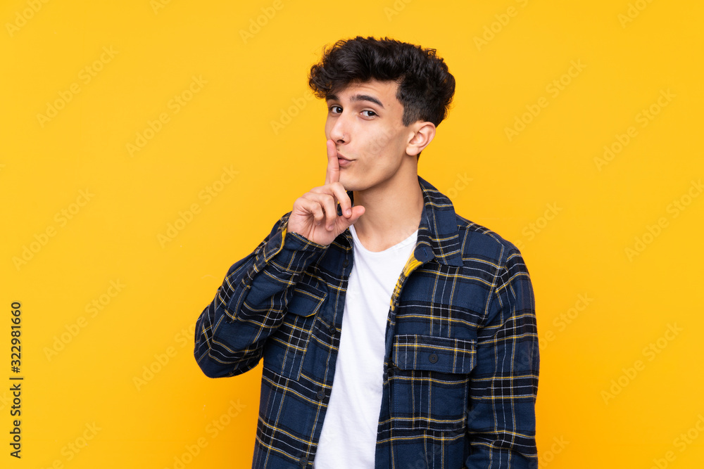 Young Argentinian man over isolated yellow background doing silence gesture Young Argentinian man over isolated yellow background doing silence gesture