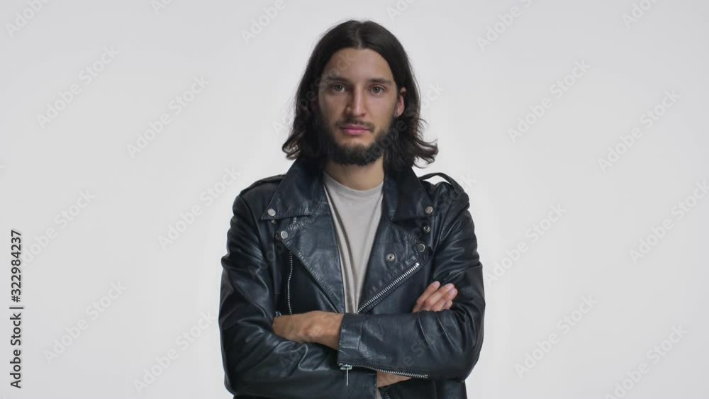 A happy young man with long hair in a black leather jacket is smiling with crossing hands isolated over white background A happy young man with long hair in a black leather jacket is smiling with crossing hands isolated over white background