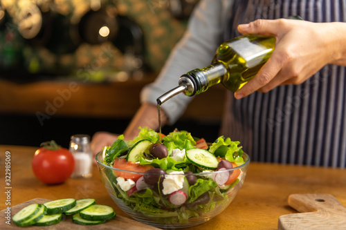 Woman chef is pouring olive oil on a glass bowl of freshly made tasty, organic diet salad. photo