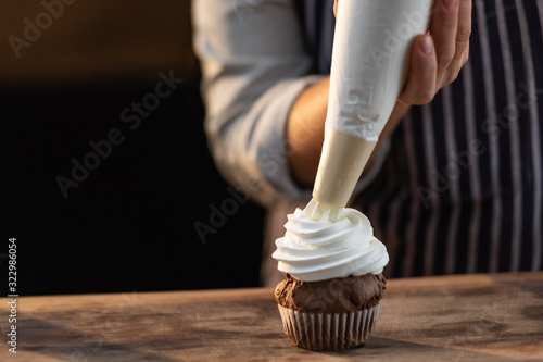 Close up of a chef pouring whipped cream over a freshly baked cupcake