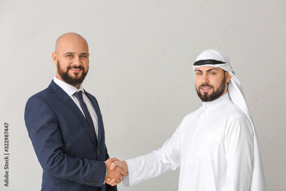 Fototapeta premium Arab man and his business partner shaking hands on grey background