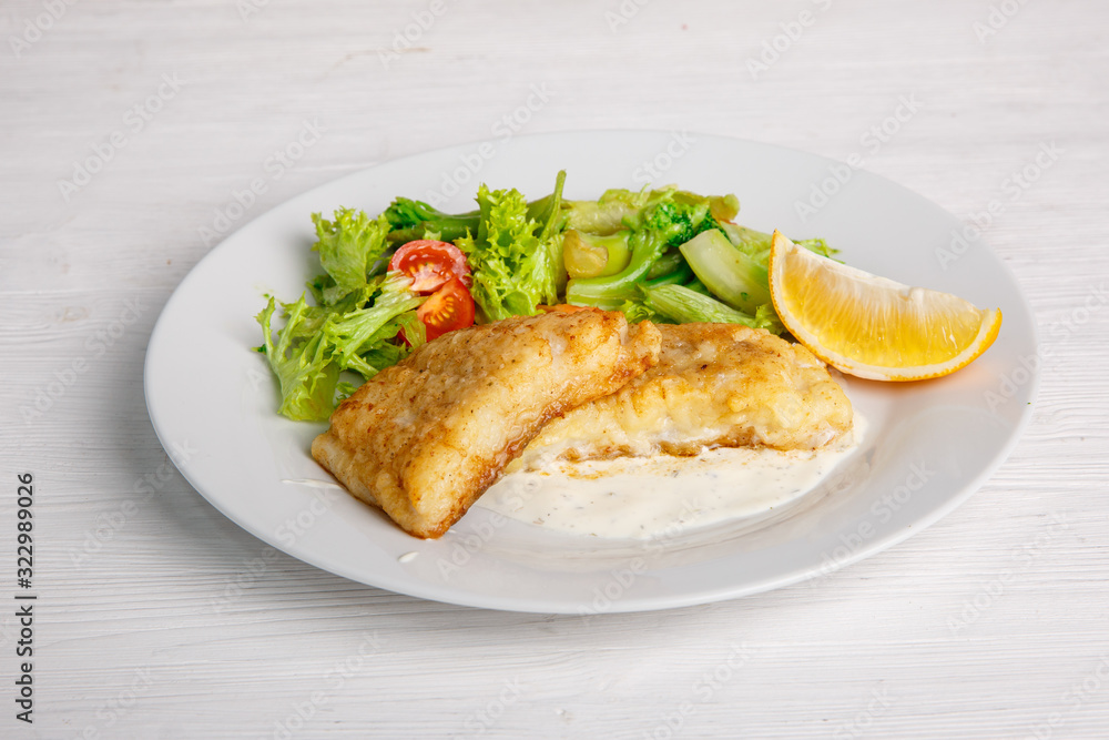 a piece of fried fish with salad leaves on a light background of the menu a piece of fried fish with salad leaves on a light background of the menu