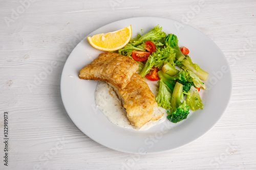 a piece of fried fish with salad leaves on a light background of the menu