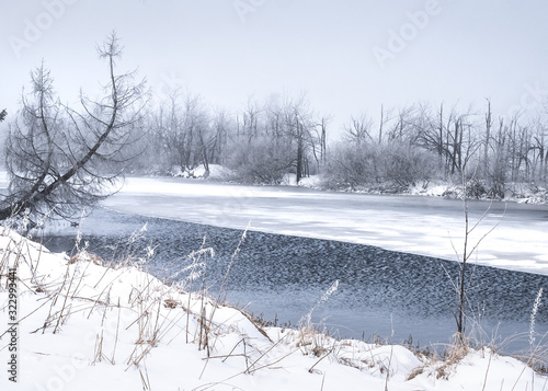Snowy winter landscape in the open countryside with a half frozen lake.