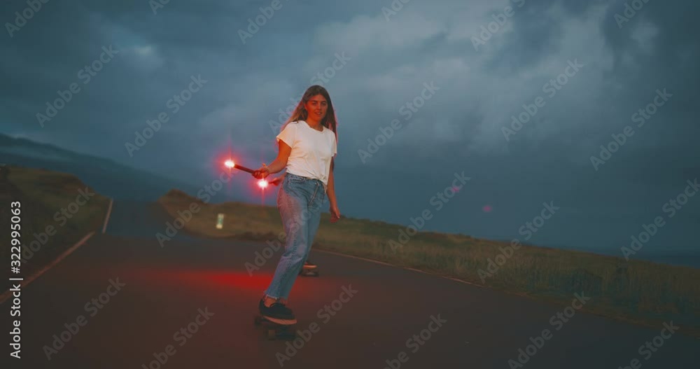 Two adventurous friends skateboarding with red glowing flares at dusk, young man and woman skateboarding together Two adventurous friends skateboarding with red glowing flares at dusk, young man and woman skateboarding together