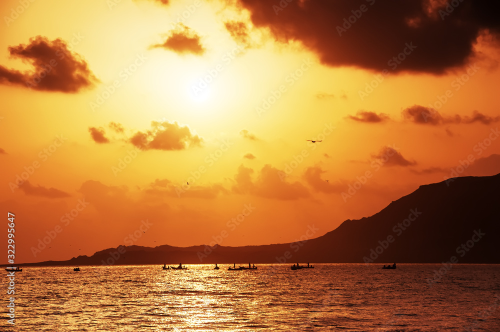 Beautiful sunrise on the coast of an island in the Indian Ocean. Village fisherman's boats in the water and the silhouette of a cliff against the background of the red dawn sky.
