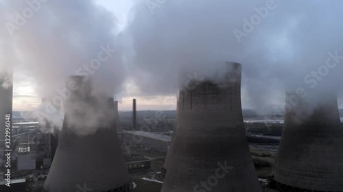 Aerial rising view of UK power station cooling towers through smoke steam emissions at sunrise.