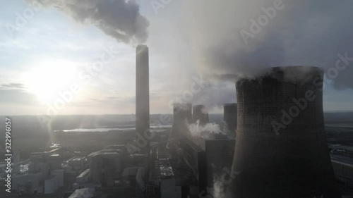 Aerial push in close to power station cooling towers through smoke steam emissions at sunrise.