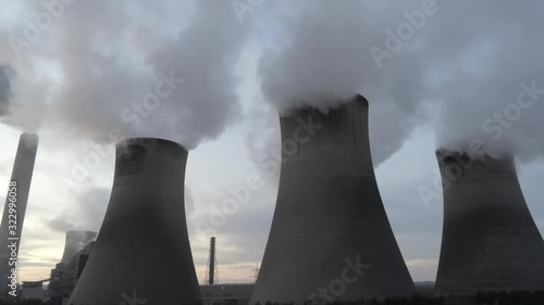Rising aerial view of UK power station cooling towers smoke steam emissions at sunrise.