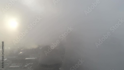 Aerial reveal view of UK power station cooling towers through smoke steam emissions during sunrise.