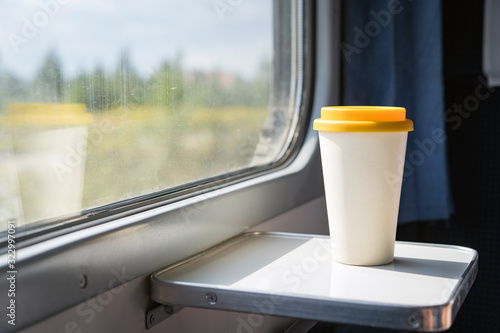 A bamboo coffee cup with a yellow silicon lid. Coffee to go on a table in the train overlooking a beautiful rural green landscape. Travel, lifestyle. Concept zero waste, reusable recyclable dishes