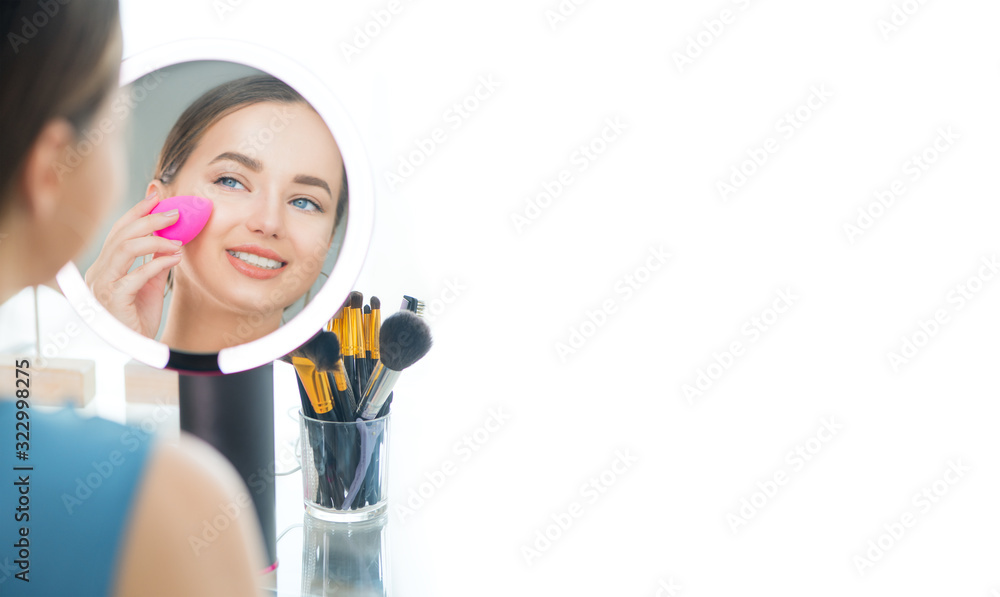 Beauty model girl applying makeup and smiling. Beautiful young woman looking in the mirror and applying cosmetic with a big brush. Happy Girl gets blush on the cheekbones. Powder, rouge Beauty model girl applying makeup and smiling. Beautiful young woman looking in the mirror and applying cosmetic with a big brush. Happy Girl gets blush on the cheekbones. Powder, rouge