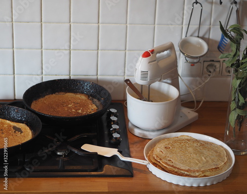 Spring, we meet Maslenitsa. Seeing off winter. Cooking pancakes on a gas stove. Next to the dough and ready-made pancakes.