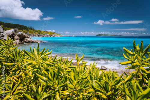 Fototapeta Naklejka Na Ścianę i Meble -  Tropical coast at La Digue island, Seychelles. Lush green vegetation, turquoise blue ocean and lonely yacht boat in background